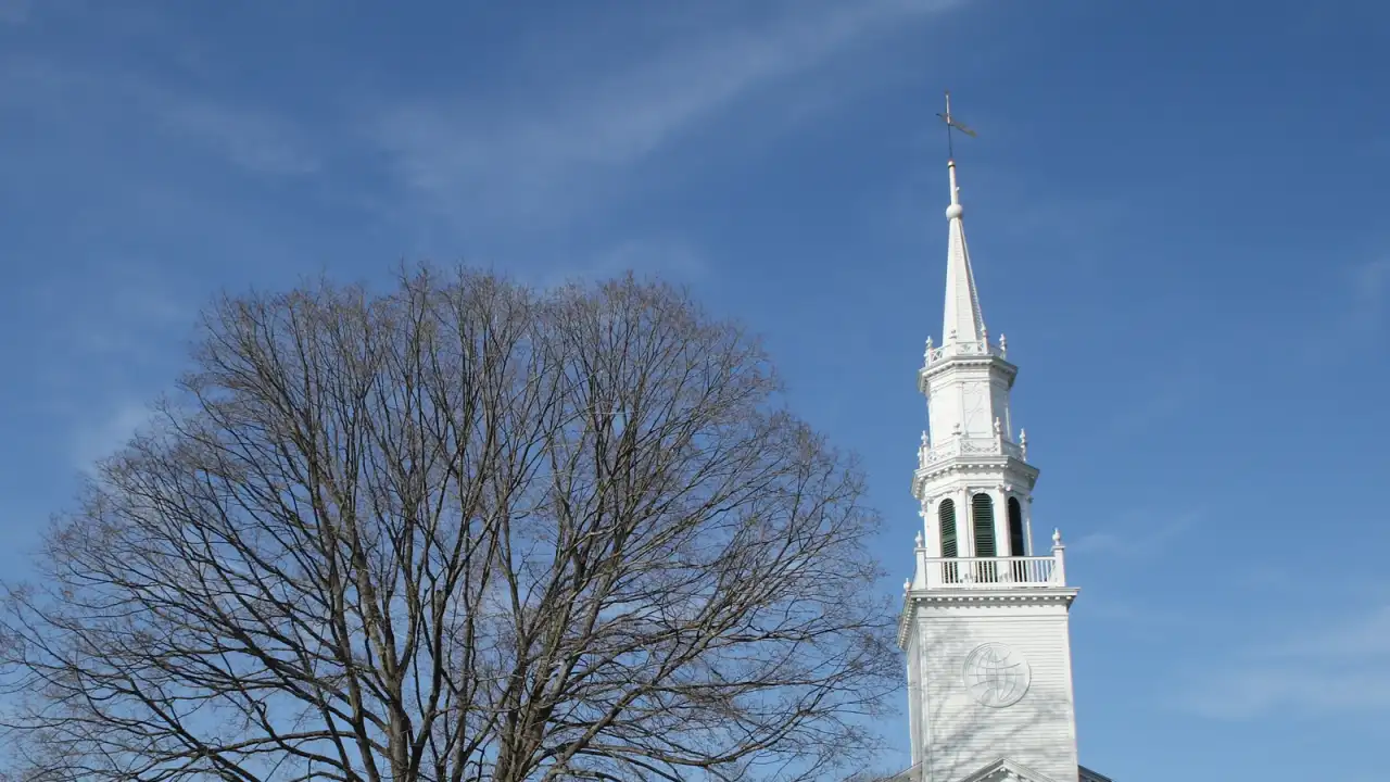 The white-steepled Avon Congregational Church beside a bare shade tree on the town green in Avon, Connecticut
